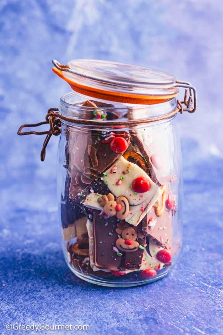 Pieces of Christmas bark, melted chocolate with pretzels and candy in a glass jar.
