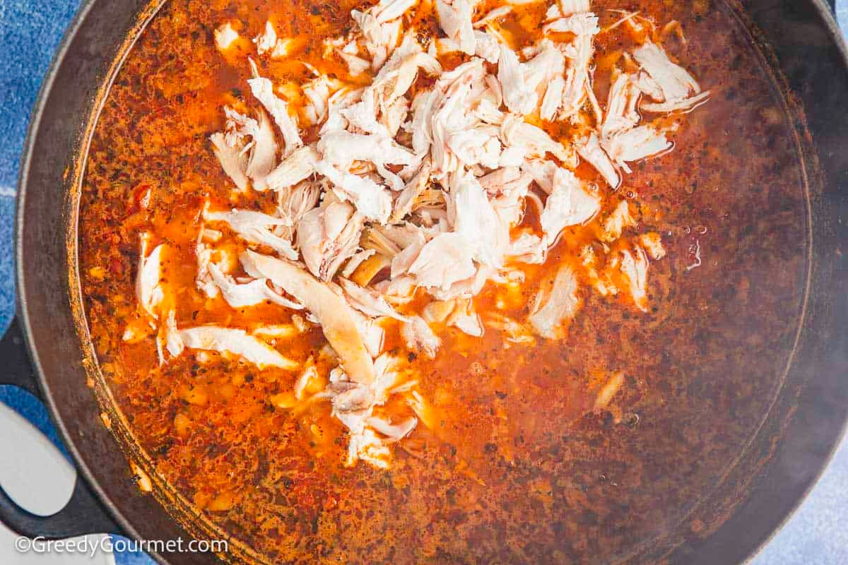 A pot of chicken, stock, pasta, tomato and chopped onion.