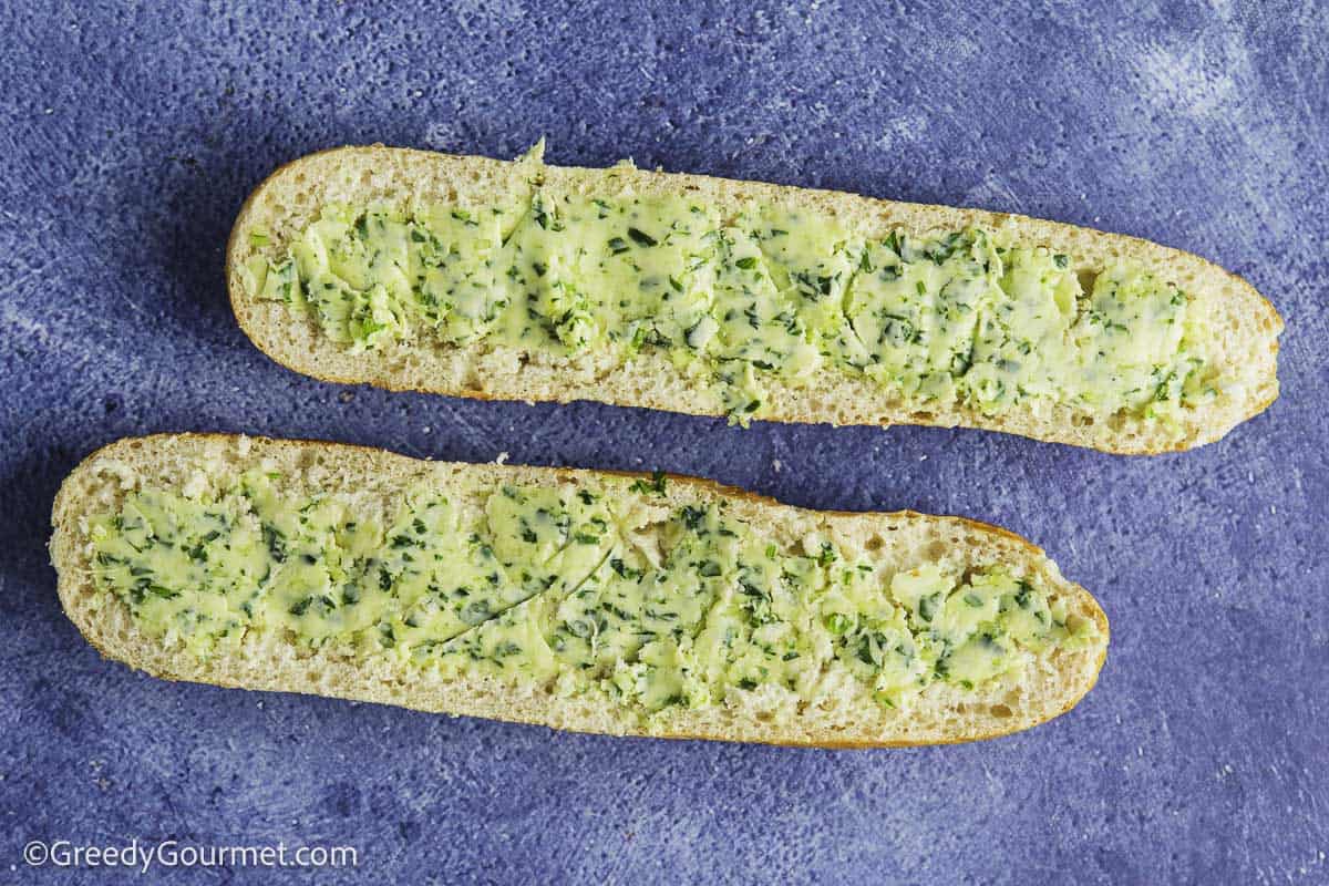 A baguette cut in half sideways with garlic butter spread on top.