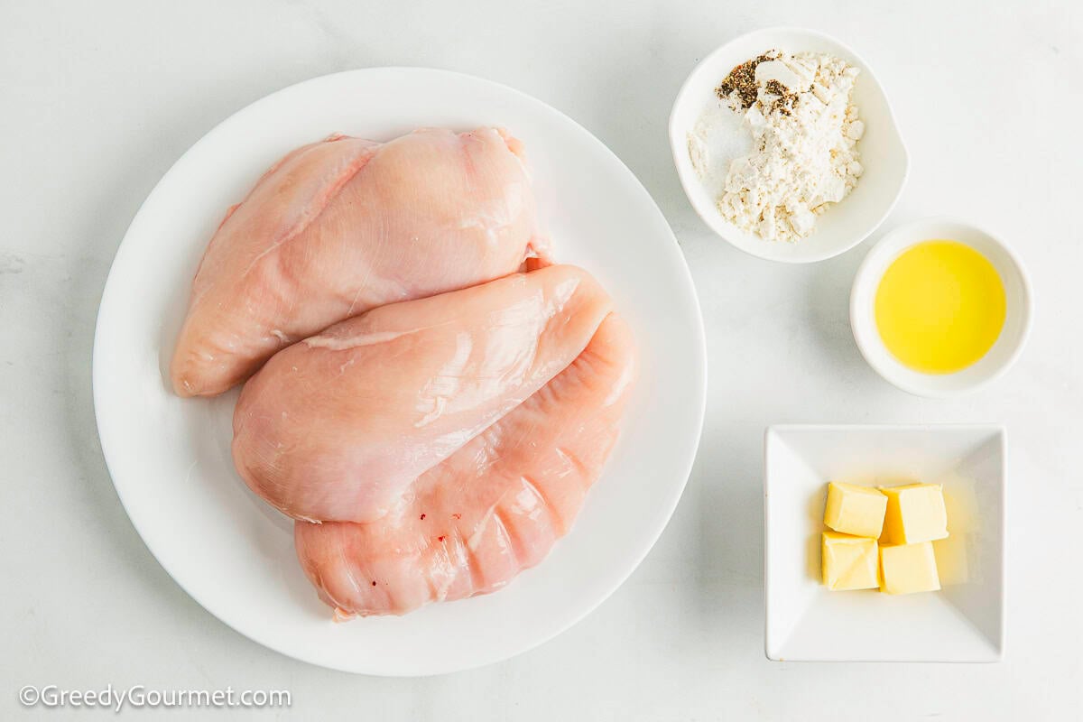 Chicken, flour, butter and oil on plates on a table.