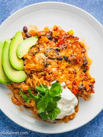 Chicken Burrito Casserole on a plate served with sour cream and avocado.