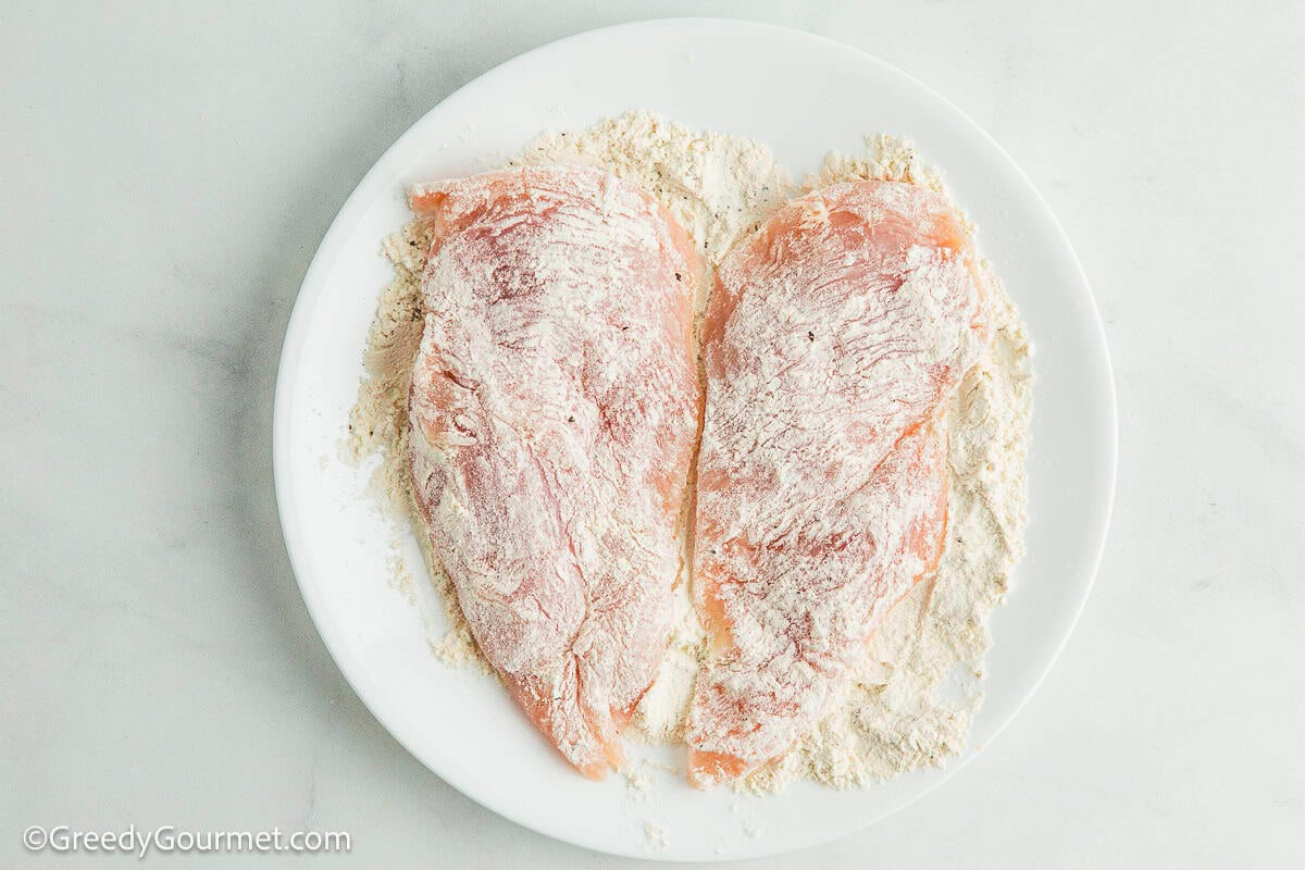 Chicken breast covered in flour on a plate.
