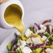 Salad dressing being poured onto a Greek salad.