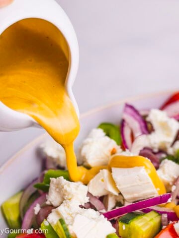 Salad dressing being poured onto a Greek salad.