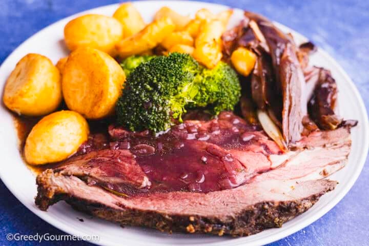 Red wine gravy drizzled on a plate with roast beef, potatoes and broccoli.