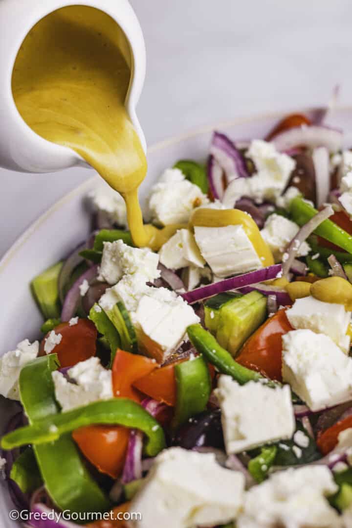Salad dressing being poured onto a Greek salad.
